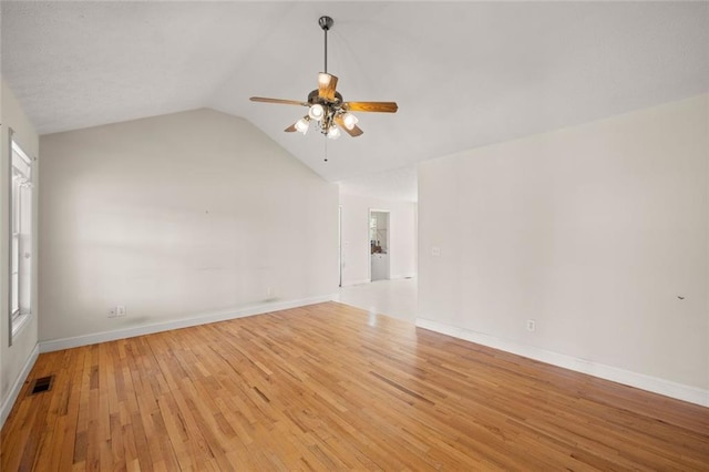 empty room with visible vents, light wood-style floors, baseboards, a ceiling fan, and vaulted ceiling