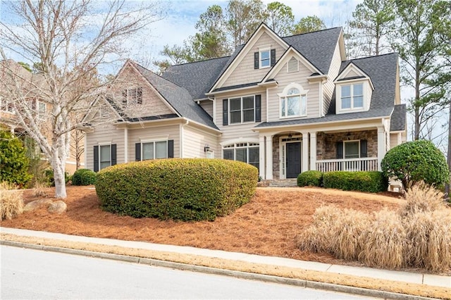 craftsman house with stone siding, a shingled roof, and covered porch