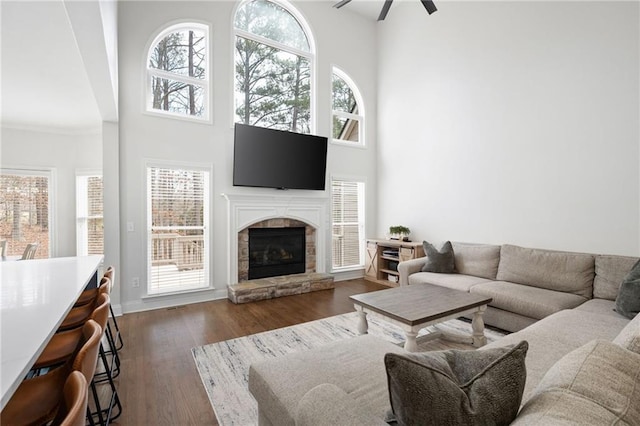 living room featuring a high ceiling, dark wood finished floors, a ceiling fan, and a stone fireplace