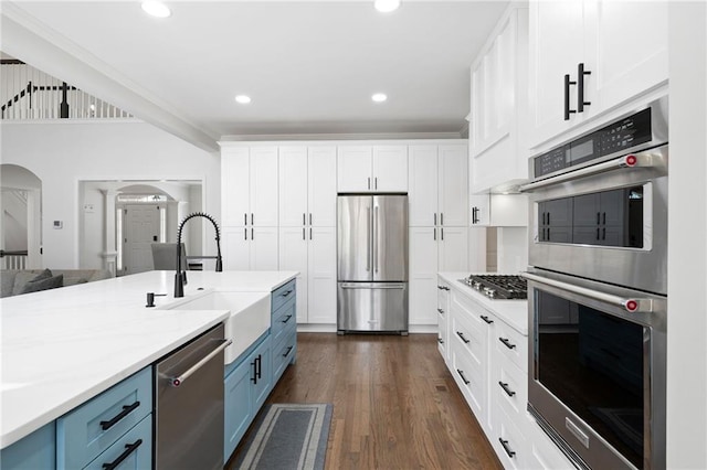 kitchen with arched walkways, blue cabinets, a sink, white cabinets, and appliances with stainless steel finishes