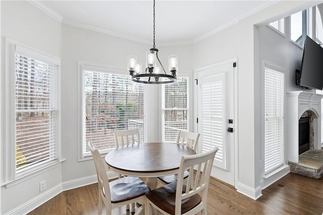 dining room with crown molding, a chandelier, a fireplace with raised hearth, and wood finished floors