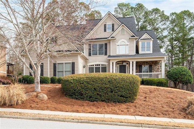 view of front of house featuring stone siding, a shingled roof, and covered porch