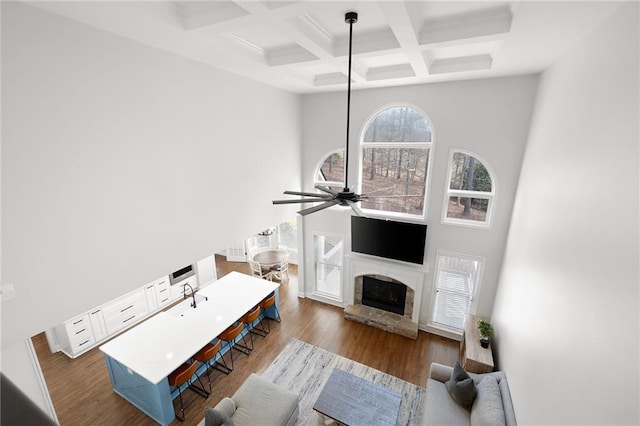 living room with a towering ceiling, ceiling fan, beamed ceiling, wood finished floors, and a stone fireplace