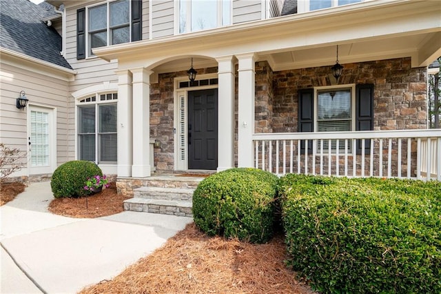 entrance to property featuring a shingled roof, stone siding, and a porch