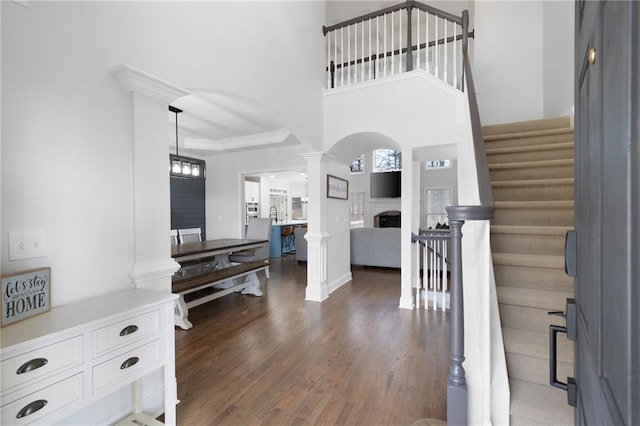 foyer entrance with arched walkways, a fireplace, decorative columns, stairway, and wood finished floors