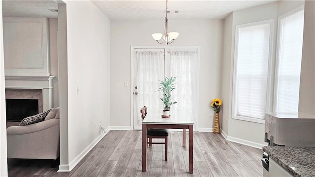 dining space with light wood finished floors, a chandelier, baseboards, and a fireplace
