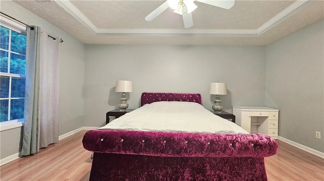 bedroom with light wood-style flooring, a tray ceiling, ornamental molding, baseboards, and a ceiling fan