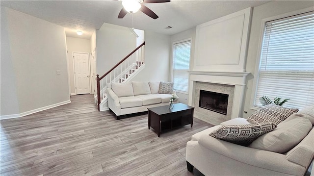 living room featuring a ceiling fan, light wood-style floors, a fireplace, stairway, and baseboards