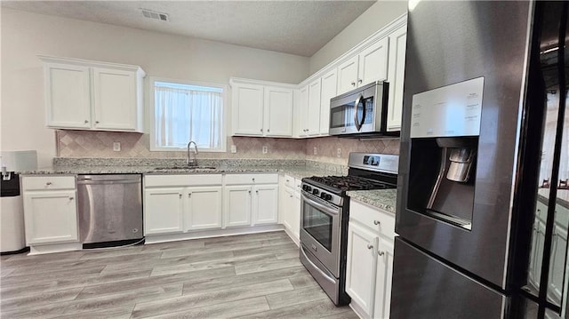 kitchen with stainless steel appliances, a sink, light stone counters, white cabinetry, and light wood-type flooring