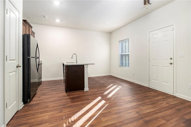 kitchen with black refrigerator, a kitchen island with sink, dark hardwood / wood-style floors, and sink