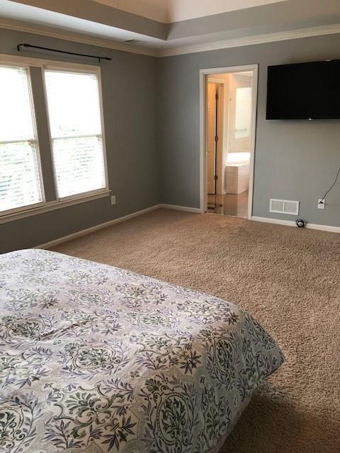 carpeted bedroom featuring ensuite bath and ornamental molding