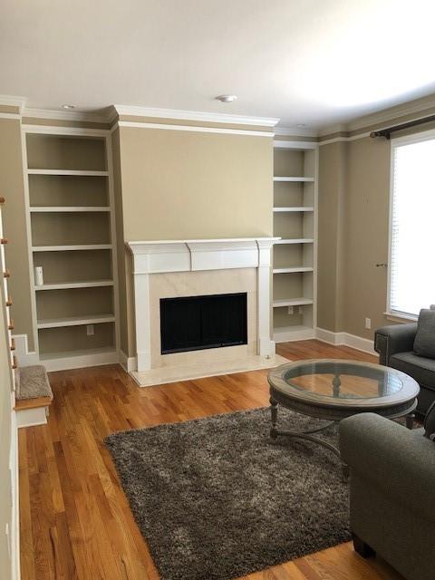 living room with built in features, wood-type flooring, a high end fireplace, and crown molding