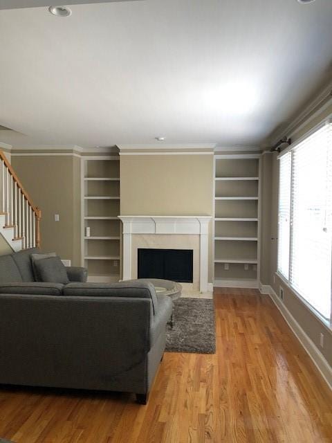 living room featuring built in features, hardwood / wood-style flooring, and crown molding