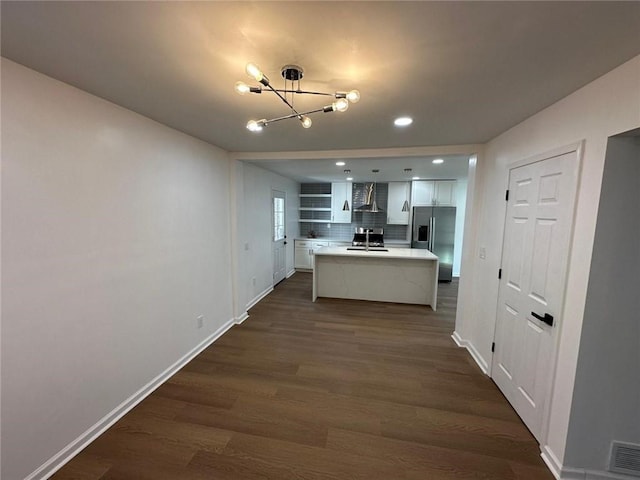 kitchen featuring dark wood-type flooring, stainless steel appliances, an island with sink, white cabinets, and wall chimney exhaust hood