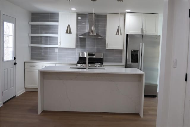 kitchen featuring white cabinetry, hanging light fixtures, a kitchen island with sink, stainless steel appliances, and wall chimney range hood