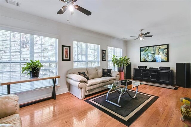 living room featuring ornamental molding, light wood-type flooring, ceiling fan, and a healthy amount of sunlight