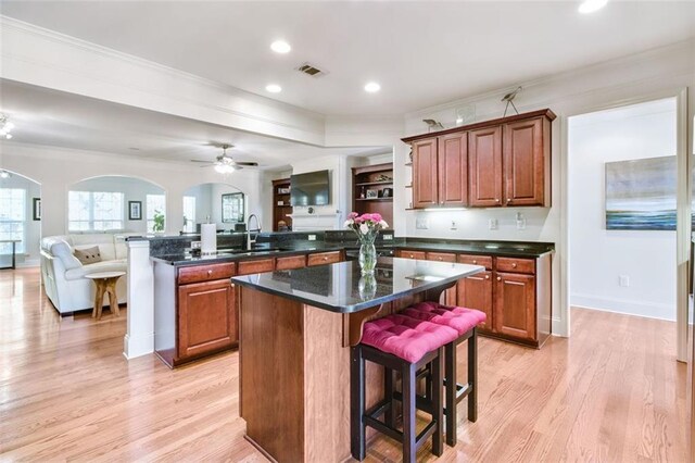 kitchen with dark stone counters, a kitchen bar, sink, light hardwood / wood-style floors, and a center island