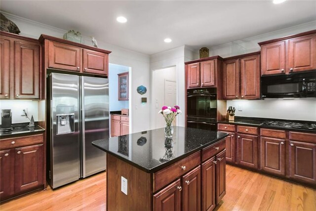 kitchen featuring black appliances, crown molding, light hardwood / wood-style floors, and a center island