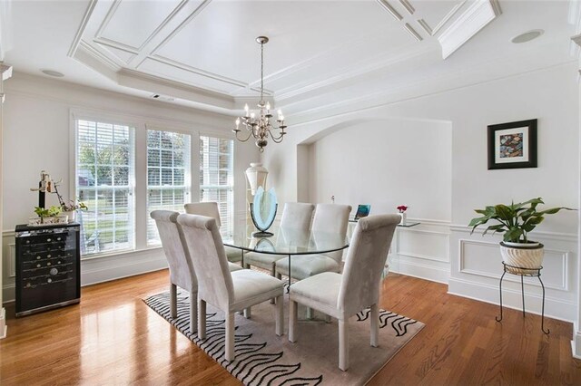 dining space featuring ornamental molding, wood-type flooring, a raised ceiling, and an inviting chandelier