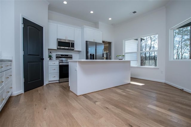 90 Ayers Rd, Bowdon, GA 30108 - kitchen featuring appliances with stainless steel finishes, white cabinets, light wood-style flooring, ornamental molding, and an island with sink