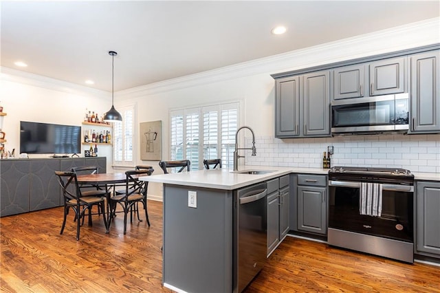 kitchen with gray cabinetry, appliances with stainless steel finishes, a sink, wood finished floors, and a peninsula