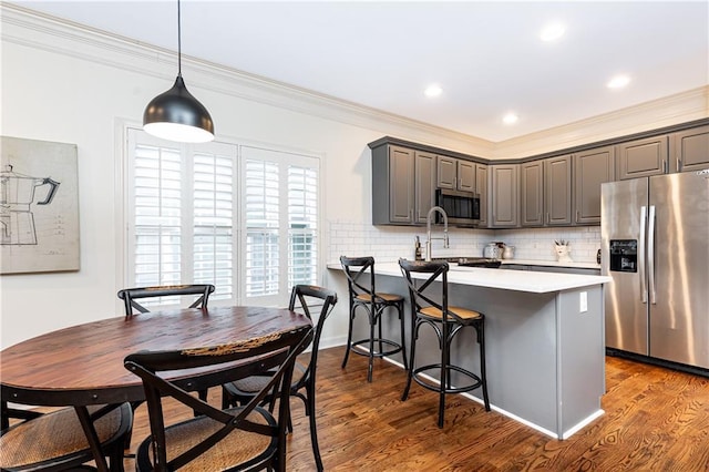 kitchen with appliances with stainless steel finishes, a kitchen breakfast bar, gray cabinets, and dark wood-style flooring