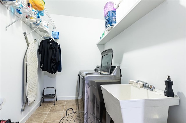 clothes washing area with laundry area, light tile patterned floors, baseboards, washer and dryer, and a sink