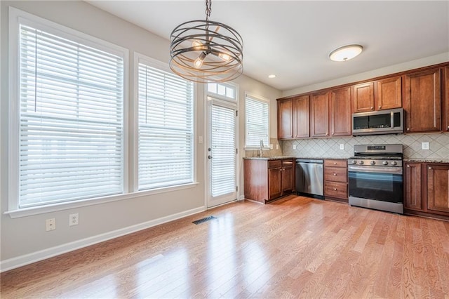 4404 Village Field Pl, Suwanee, GA 30024 - kitchen with appliances with stainless steel finishes, a chandelier, light wood finished floors, decorative backsplash, and brown cabinetry