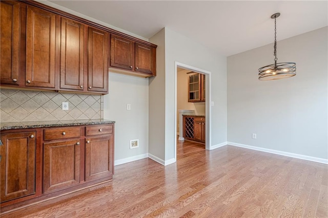 4404 Village Field Pl, Suwanee, GA 30024 - kitchen featuring light wood finished floors, tasteful backsplash, dark stone counters, hanging light fixtures, and baseboards
