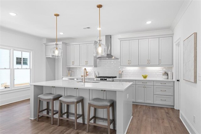 kitchen featuring pendant lighting, wall chimney range hood, hardwood / wood-style flooring, stainless steel range, and white cabinetry