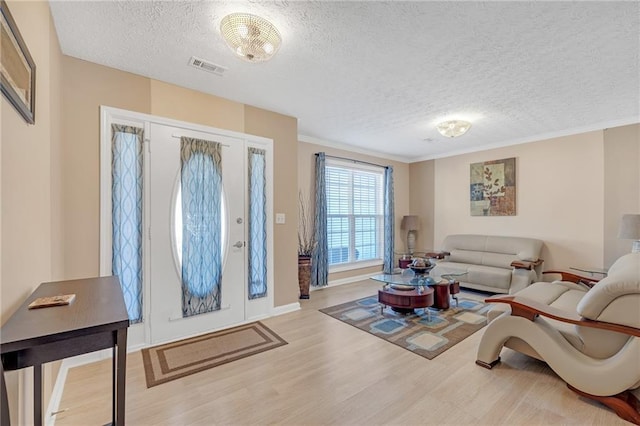 living room with a textured ceiling, visible vents, wood finished floors, and ornamental molding