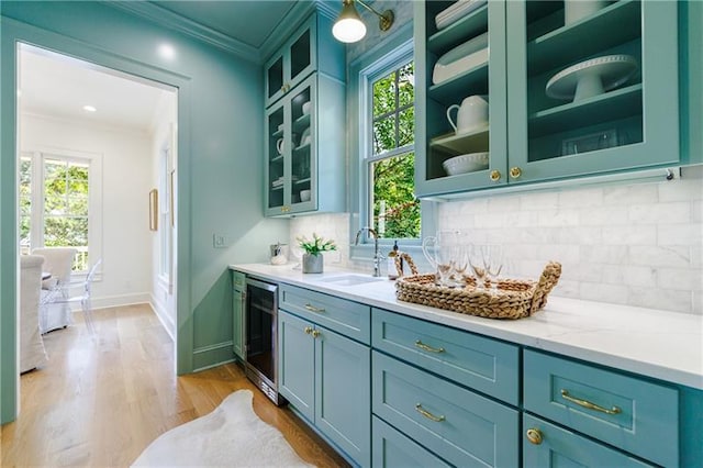 bar featuring decorative backsplash, light stone counters, beverage cooler, sink, and light hardwood / wood-style floors