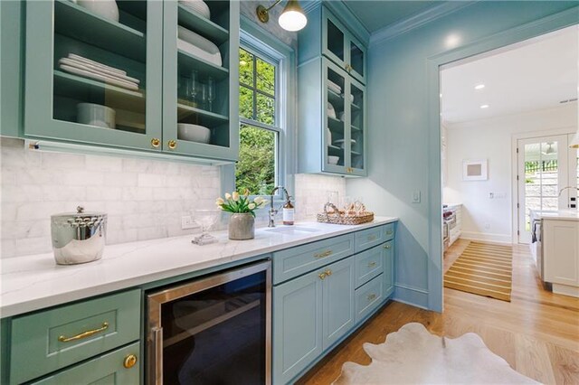 bar featuring light stone countertops, sink, beverage cooler, light hardwood / wood-style flooring, and ornamental molding