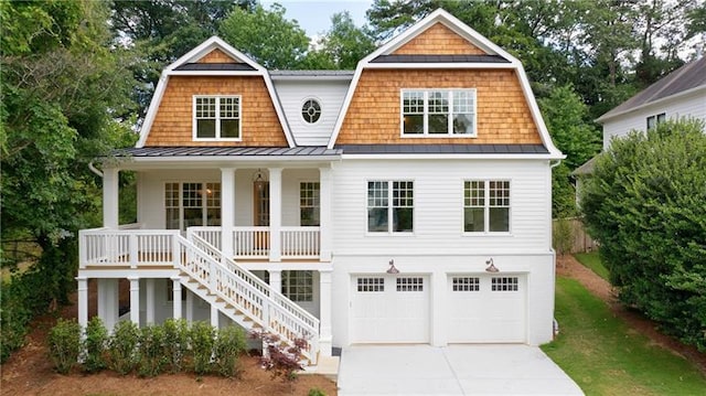 shingle-style home featuring a porch, a gambrel roof, stairs, concrete driveway, and a standing seam roof