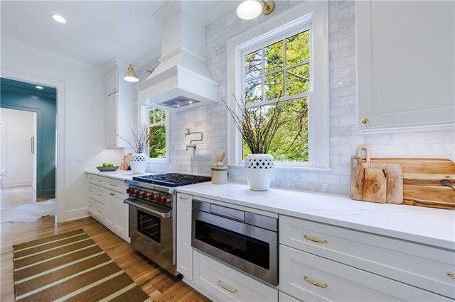 kitchen featuring high end stainless steel range oven, white cabinets, custom range hood, and built in microwave