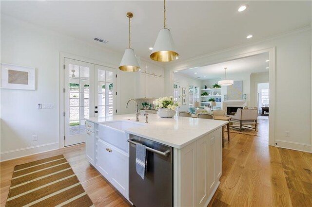 kitchen with french doors, hanging light fixtures, stainless steel dishwasher, a center island with sink, and white cabinets