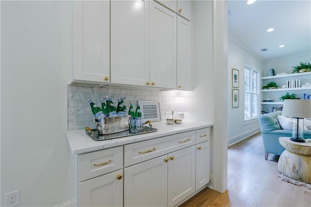 bar featuring decorative backsplash, crown molding, white cabinets, and light wood-type flooring