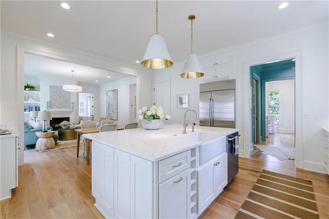 kitchen featuring sink, hanging light fixtures, stainless steel appliances, a kitchen island with sink, and white cabinets