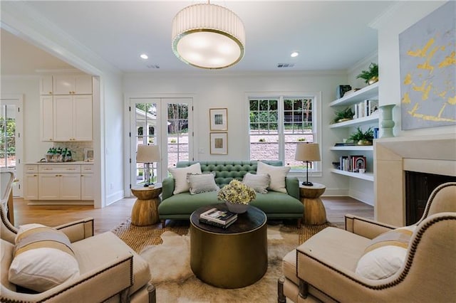 sitting room with built in shelves, light hardwood / wood-style floors, and ornamental molding