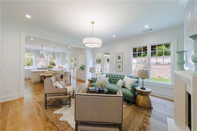 living room with light hardwood / wood-style flooring, a premium fireplace, crown molding, and french doors