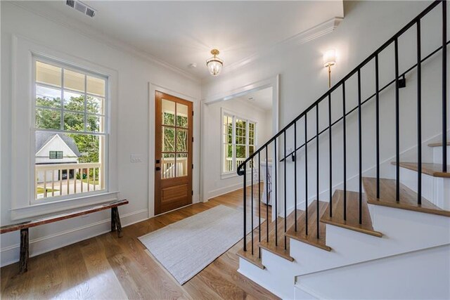 foyer with wood-type flooring, an inviting chandelier, crown molding, and a healthy amount of sunlight