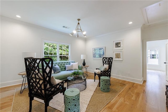 living room with crown molding, an inviting chandelier, and light wood-type flooring