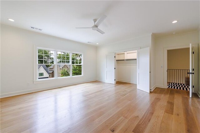 unfurnished bedroom with a spacious closet, a closet, light hardwood / wood-style flooring, and ceiling fan