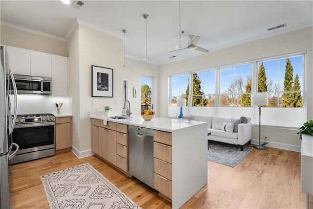 kitchen with stainless steel appliances, visible vents, light wood-style flooring, ornamental molding, and a peninsula