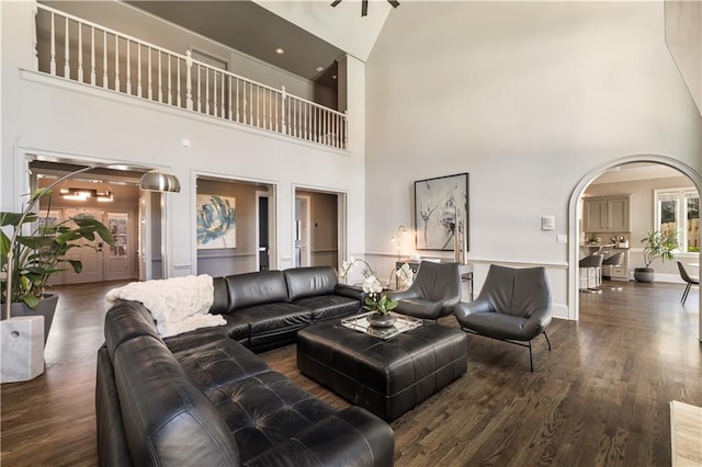 living room featuring a towering ceiling, arched walkways, baseboards, and wood finished floors