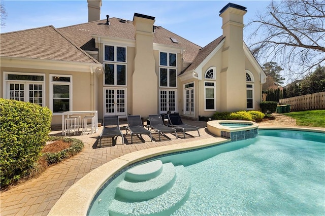 view of pool with fence, a pool with connected hot tub, a patio area, and french doors