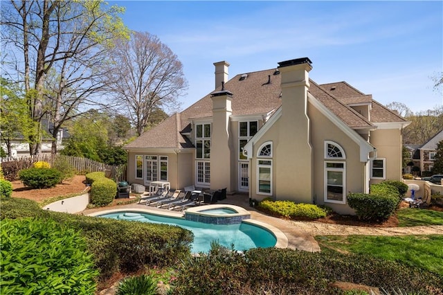 rear view of house featuring a pool with connected hot tub, a patio area, a chimney, stucco siding, and fence
