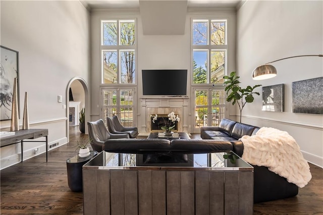 living room featuring crown molding, a healthy amount of sunlight, dark wood finished floors, a high ceiling, and a tiled fireplace