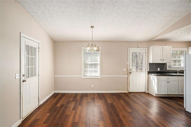 unfurnished dining area featuring dark wood-style floors, a notable chandelier, and baseboards