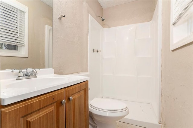 bathroom featuring a shower, a textured wall, vanity, and toilet